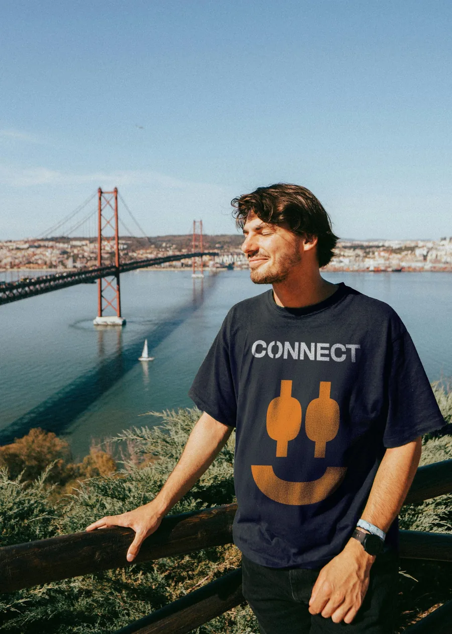 A navy Connect T-shirt with an orange face drawn from the split O, above the Tagus bridge in Lisbon